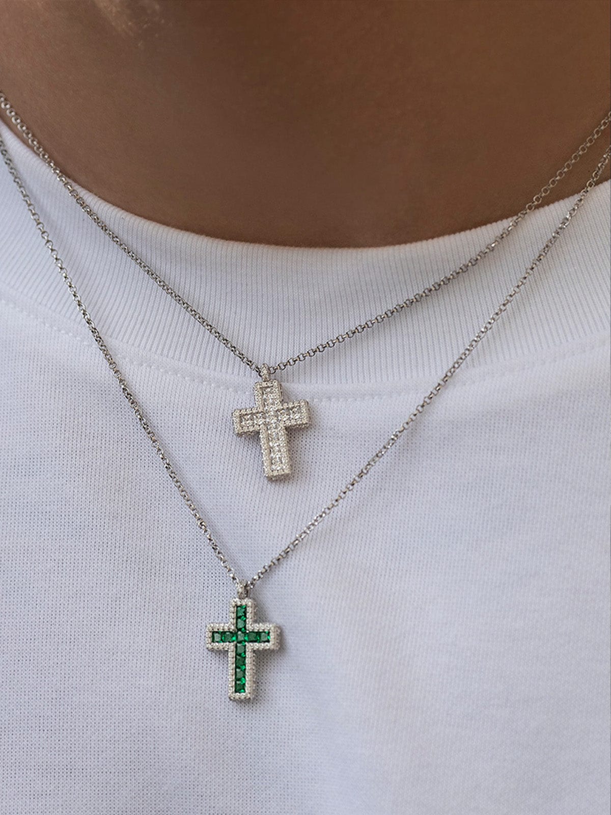 Two cross-shaped necklaces on a white shirt background