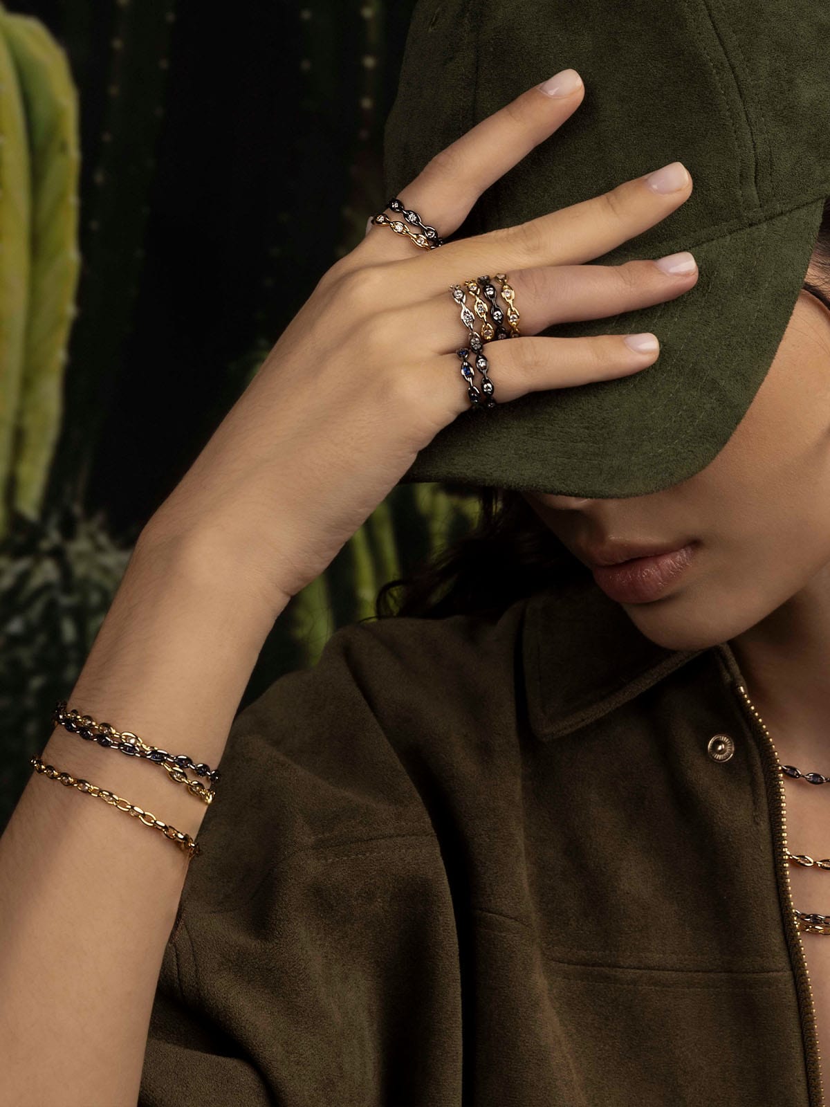 Person wearing a green apm monaco cap with jewelry on a dark background