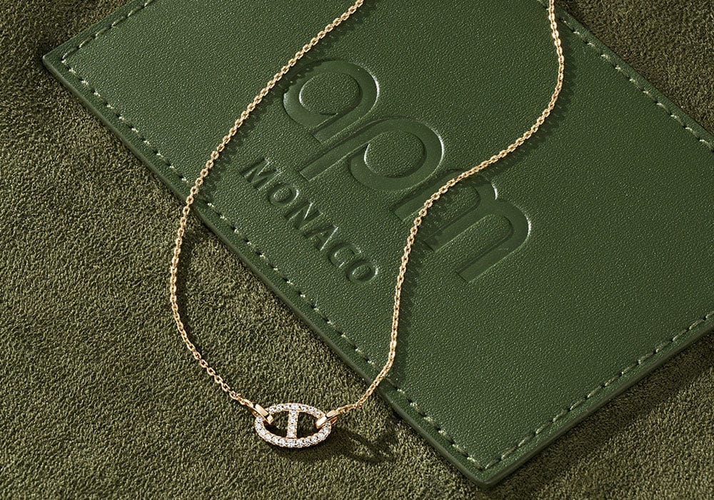 Gold yacht club necklace on a green leather surface with 'APM Monaco' 