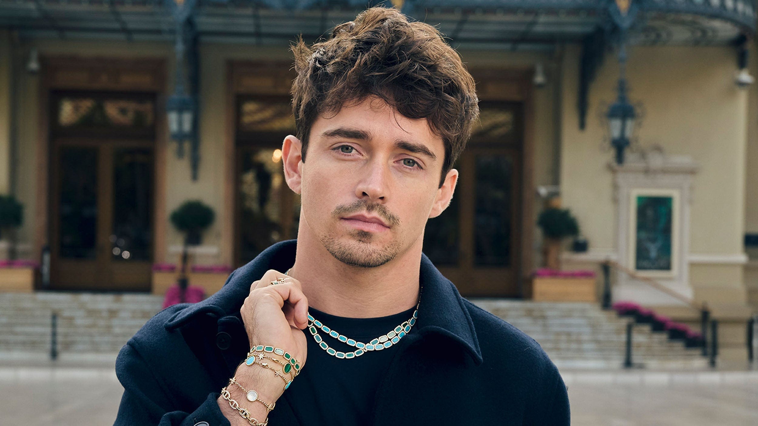 APM Monaco Collection Mediterrane Charles Leclerc wearing malachite and lagoon choker with bracelets in front of the Saint tropez casino