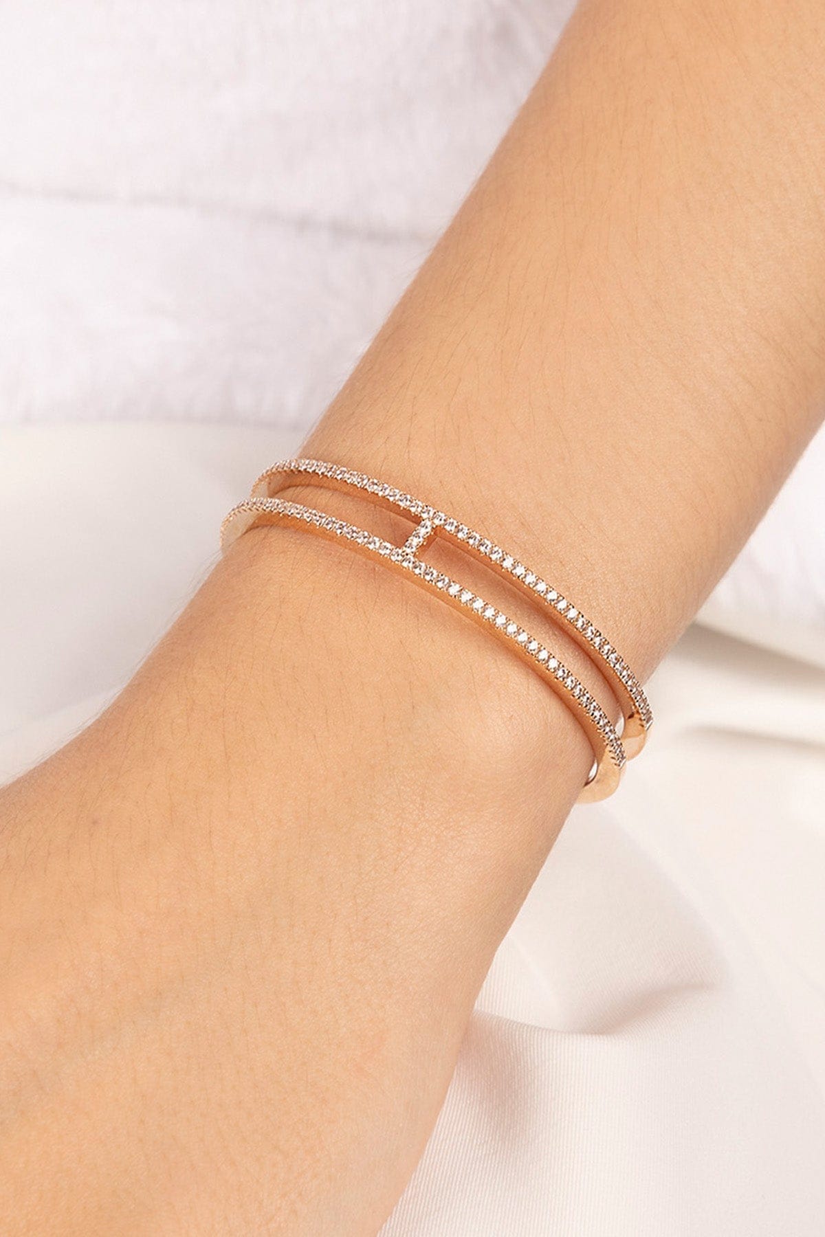 APM MONACO rose gold cuff with double-line design on a wrist with a white background