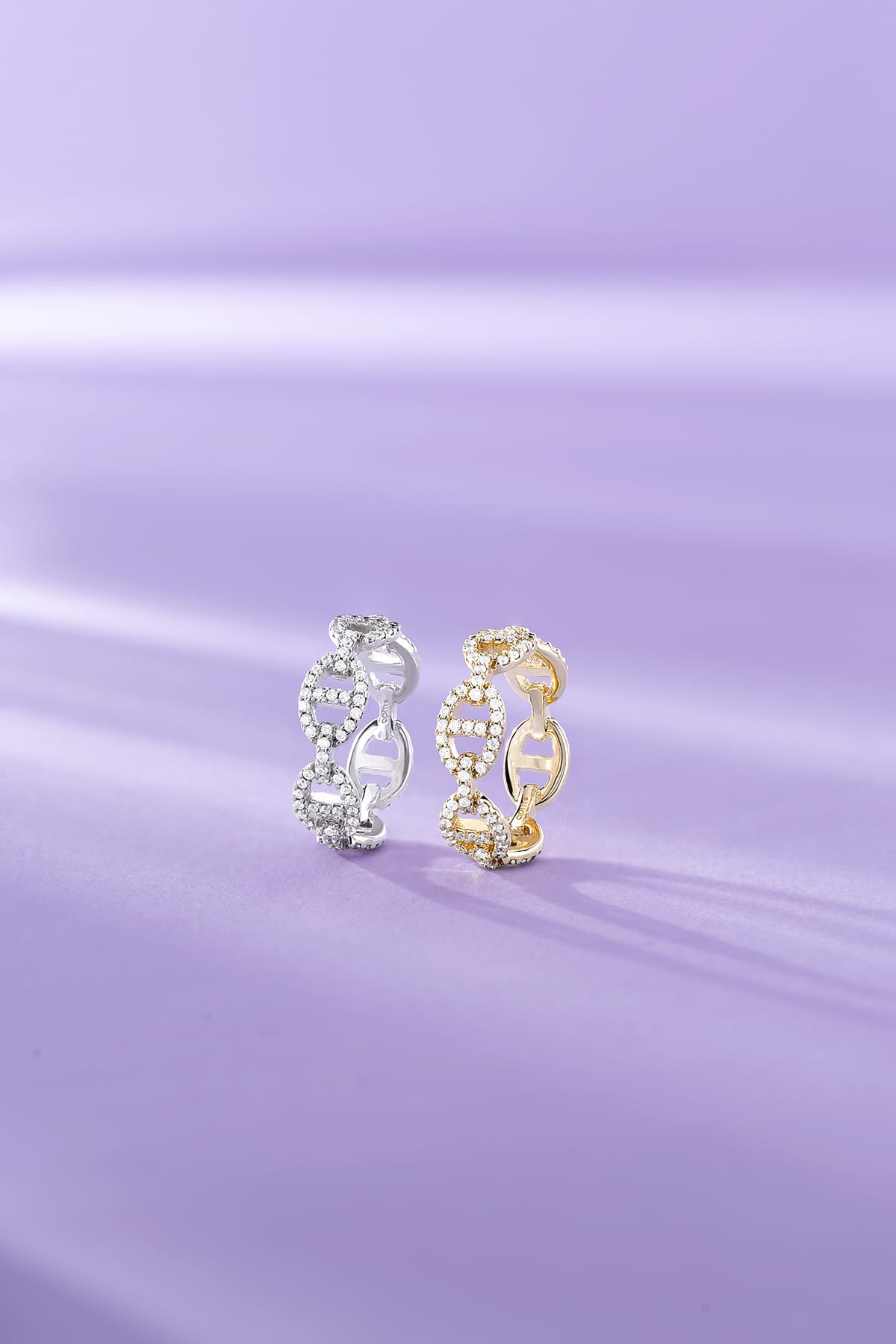 Two APM MONACO yellow gold and silver hoop earrings on a purple fabric background