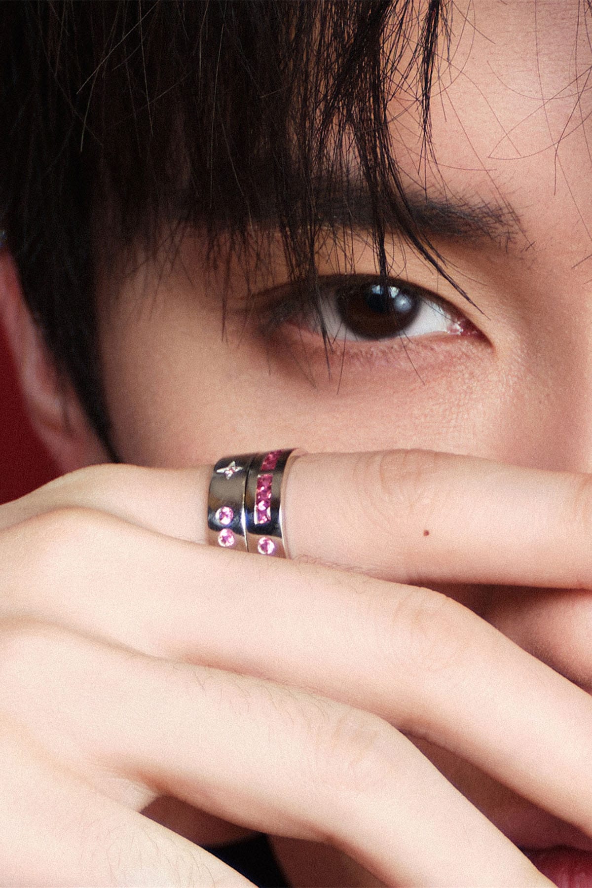 Close-up of a person wearing rings with colorful stones, covering part of their face.