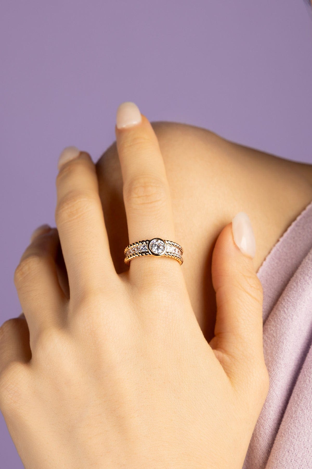 Close-up of a hand wearing a gold ring with a zirconia on a purple background