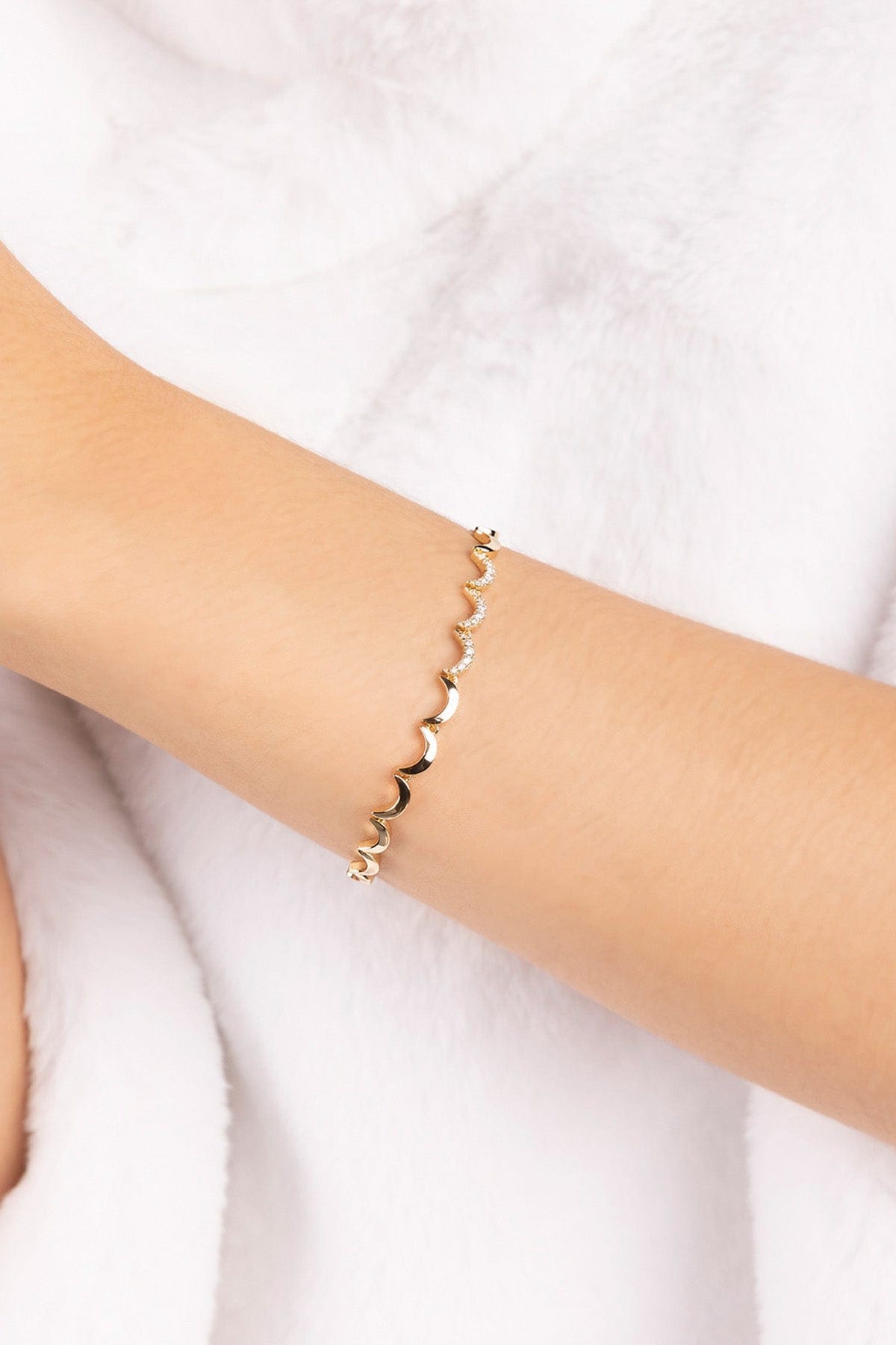 Gold plated bracelet on a person's wrist against a white background