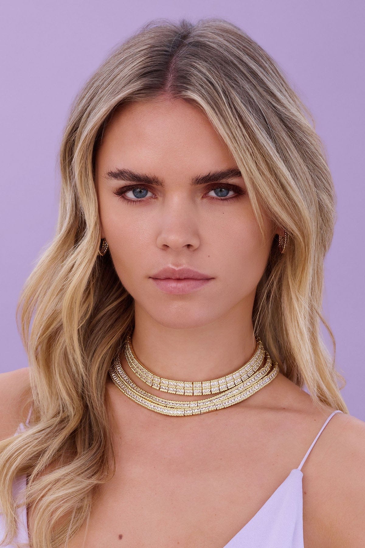 a person wearing with a decorative gold neckline against a purple background.